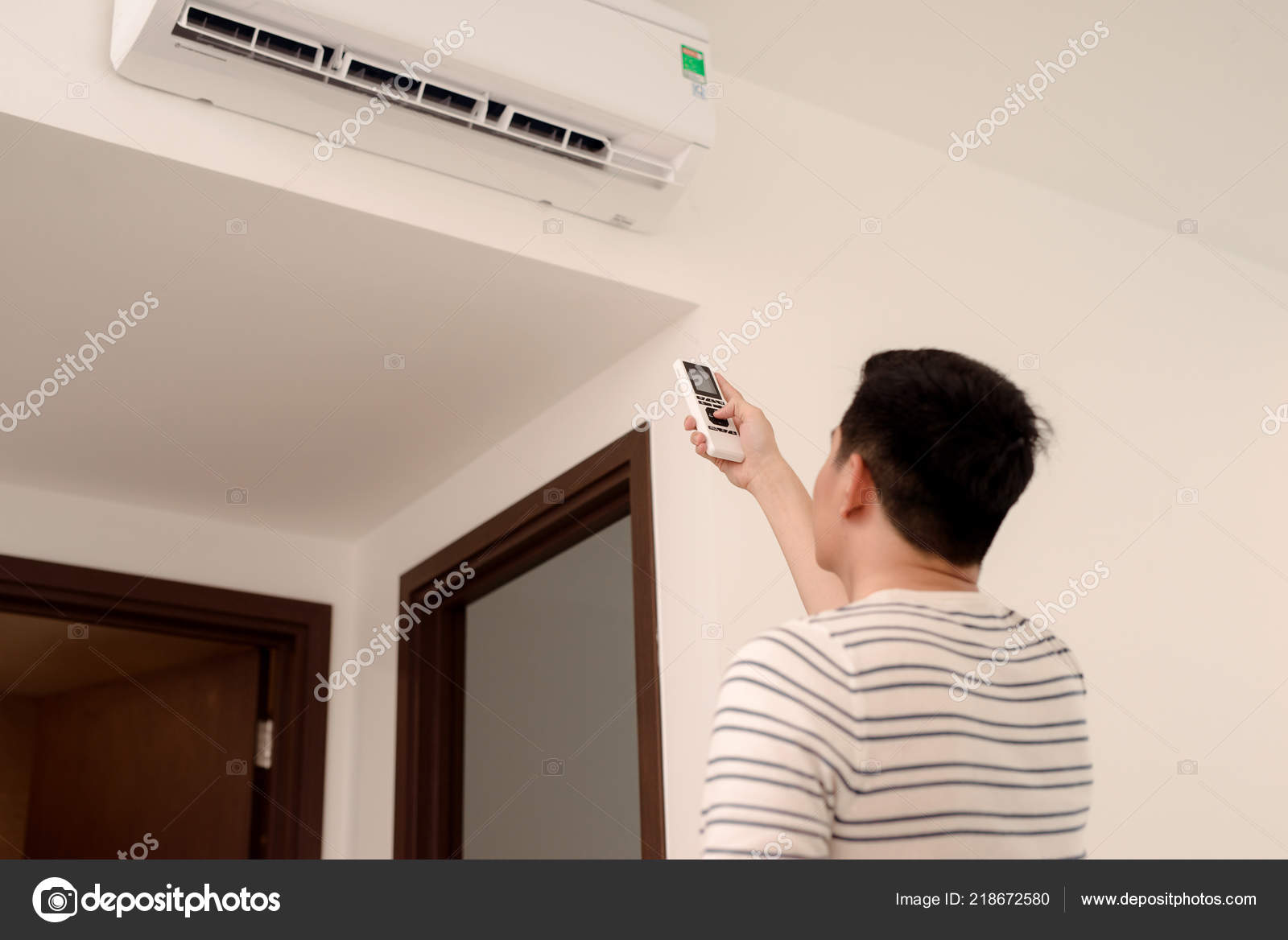 Young Man Switching Adjusting Wall Mounted Air Conditioner