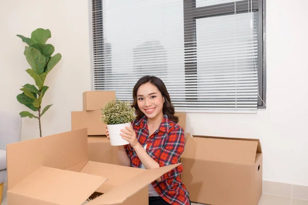 Excited young asian woman unpacking carton boxes with cozy home stuff in new apartment.