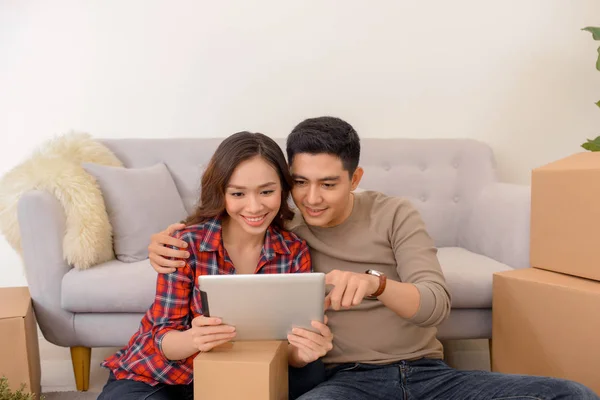 happy young couple student roommate making future project with internet computer at home while packing boxes and moving furniture during move into their new home flat apartment