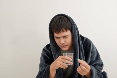 Genç bir adam grip, evde bir battaniyenin altında yatıyor, bir hap alır