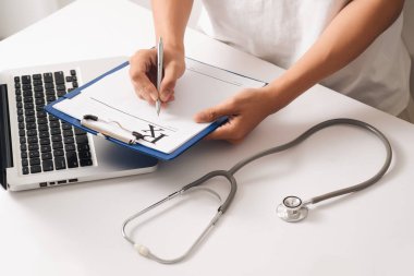 Ellerinde kapatın. Asyalı kadın doktor ile dizüstü bilgisayar ve bir şeyler yazıyor Pano, reçete, evrak, hasta denetim listesi kağıt veya uygulama formu bir hastanede.