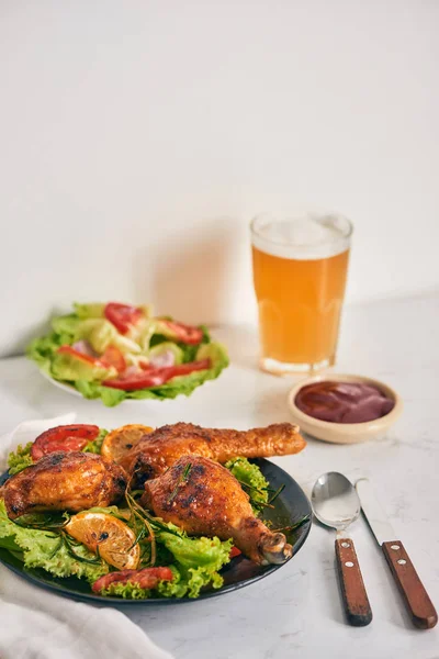 烤鸡腿烤上烤在黑盘子上的番茄酱在碗和莴苣叶 玻璃杯啤酒 — 图库照片