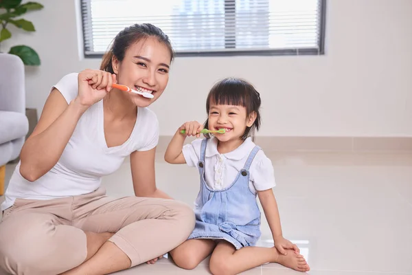 Mother and daughter brushing teeth on floor