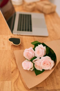 Dizüstü bilgisayar ile ahşap masa üzerinde pembe güller.