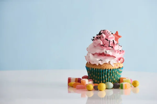 Cupcake Mit Rosa Sahneglasur Und Bonbons Auf Blauem Hintergrund — Stockfoto