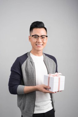 İyi bir hediye kutusu tutan genç adam arıyorum ve gri arka plan karşı dururken kamera arıyorum