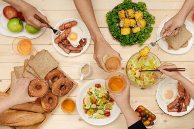 Bir grup insan ahşap masada otururken birlikte yemek yiyorlar.