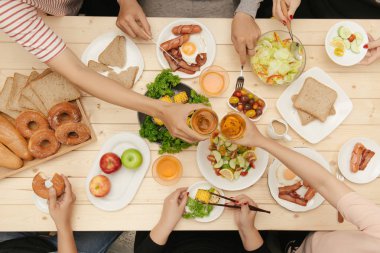 Bir grup insan ahşap masada otururken birlikte yemek yiyorlar.