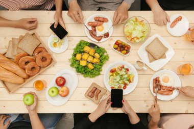 Bir grup insan ahşap masada otururken birlikte yemek yiyorlar.
