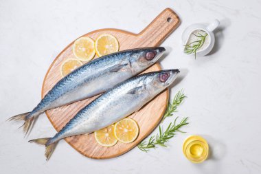 Çeşitli malzemelerle pişirme balık yemek. Limon dilimleri ve gri arka plan üzerinde otlar ile dekore edilmiş taze çiğ balık