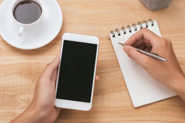 Not defteri ve kahve Kupası tahta masada Smartphone yazarken holding işadamı eller