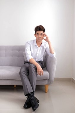 kanepede oturan ve beyaz arka plan üzerinde kameraya bakarak işadamı