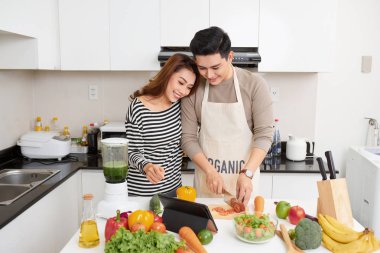 Mutlu genç çift öğle yemeği için sebze yemek hazırlarken kapalı modern mutfakta eğlenin
