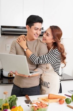 Güzel genç çift dijital tablet kullanma ve evde mutfakta yemek yaparken gülümseyen