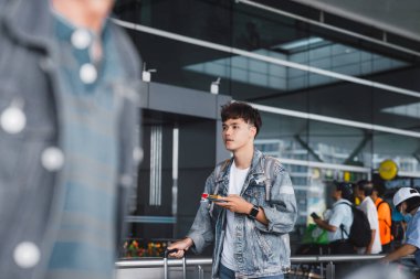 Genç aisan adam manifatura havaalanındaki bagaj arabaları satırlarının yanında dururken telefonda