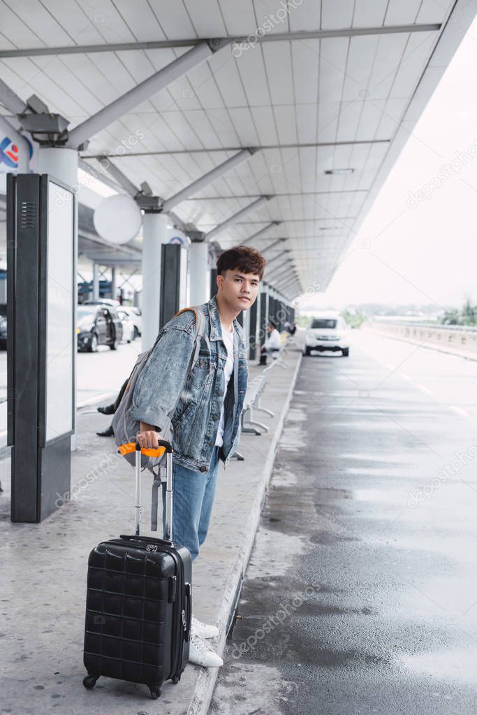 Young man pulling and use smartphone suitcase in modern airport terminal. Travelling guy with his luggage while waiting for transport