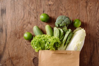 ahşap masa üzerinde alışveriş çantası içinde yeşil sebzeler