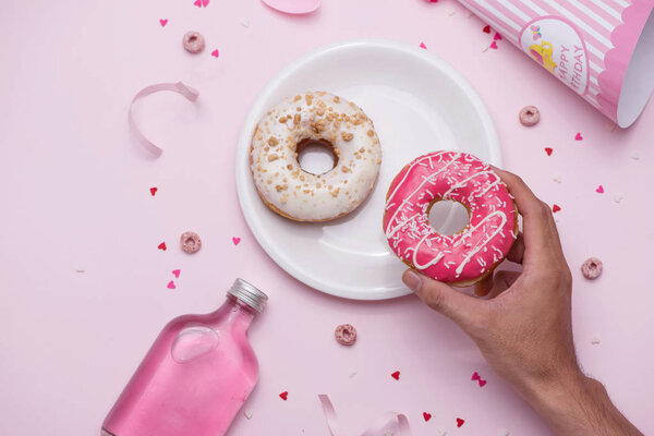 Colorful donuts on plate on pink background with human hand