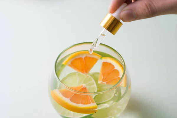 Mão Humana Deixando Cair Óleo Essencial Com Laranja Sobre Fundo — Fotografia de Stock