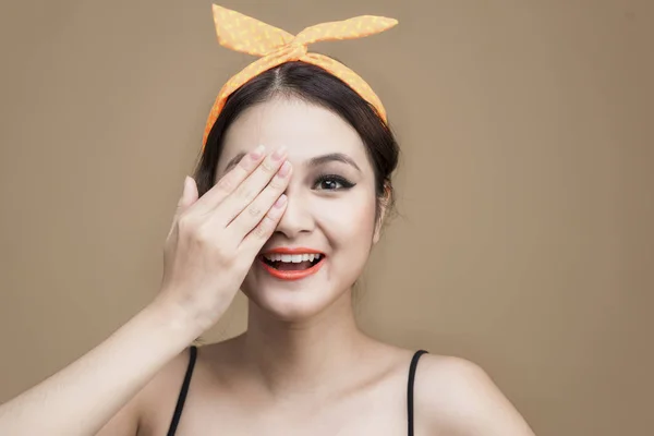Portrait of asian girl in pinup style hiding eye by hand on brown background