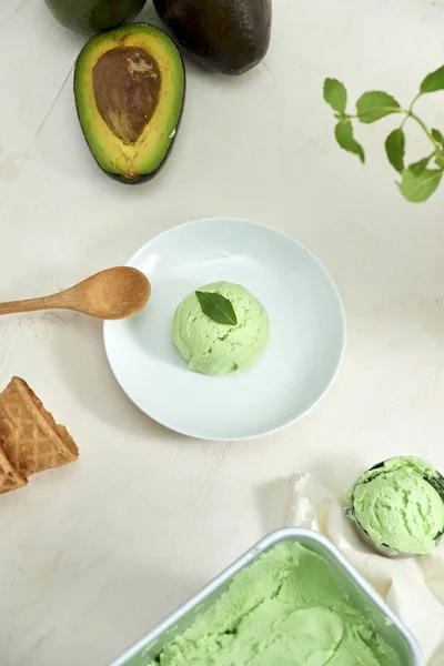 Avocado ice cream ball on white plate with wooden spoon on white background