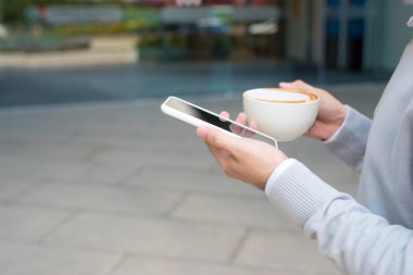 Erkek el smartphone ve holding fincan kahve kullanarak yakın çekim