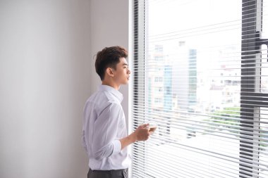 Bir fincan kahve duran ofis pencere tutarak kendine güvenen genç işadamı portresi