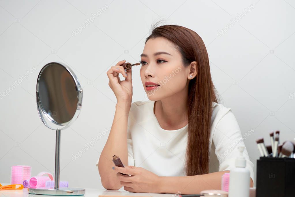 Beautiful young asian woman looking in mirror and applying mascara make-up