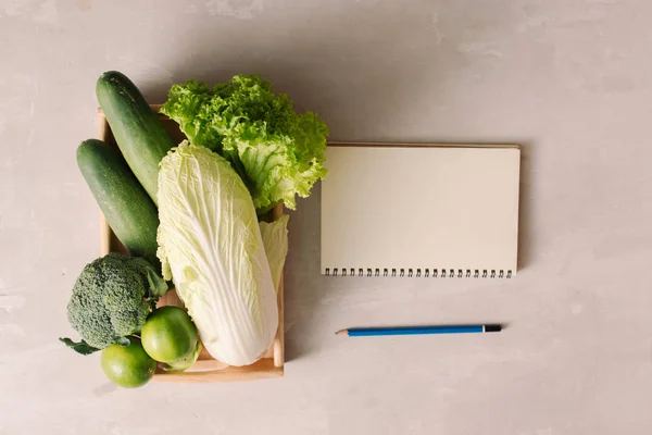 用铅笔和笔记本在白色表面的木制托盘中的新鲜蔬菜 — 图库照片