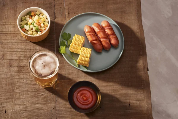 盘子里的烤香肠 沙拉和木桌上的一杯啤酒 — 图库照片
