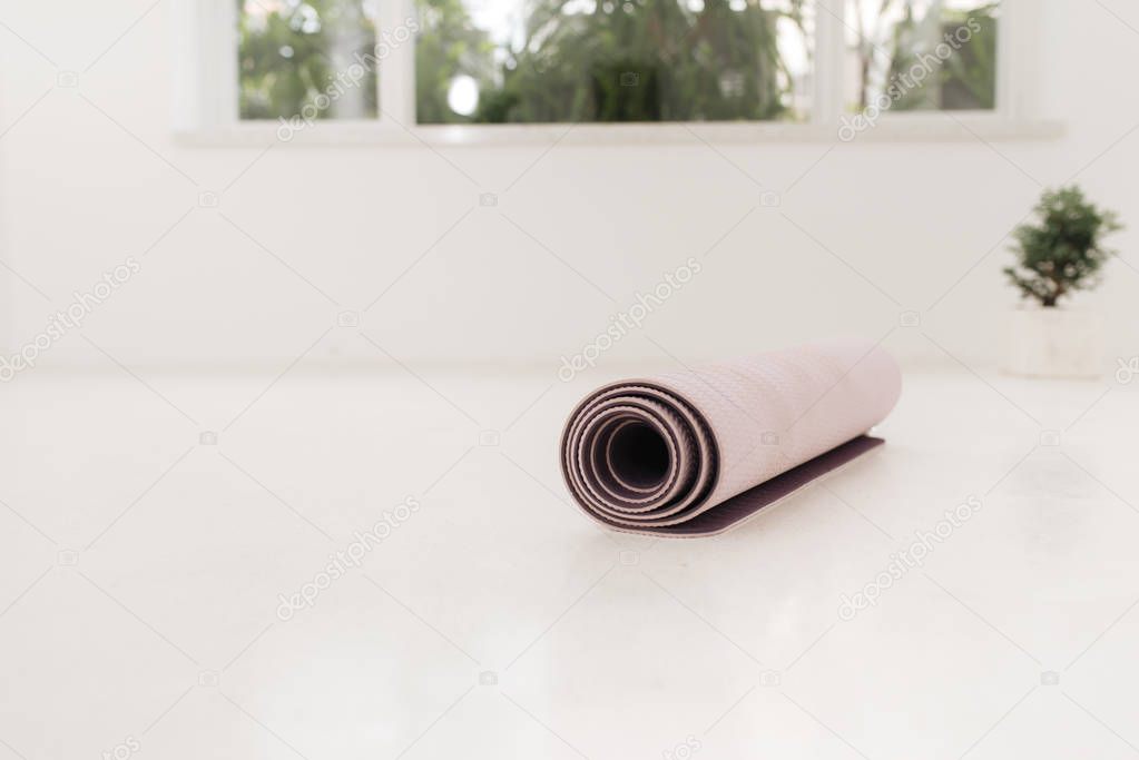 Rolled up yoga or pilates mat for exercise on natural wooden floor, sport class before or after practicing yoga, preparing for exercise