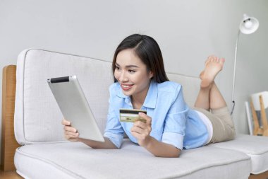 mutlu kadın oturma odasında kredi kartı ile online alışveriş için dijital tablet kullanma