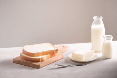 Beyaz masanın üzerine tereyağı ve süt şişeleri ile gemide beyaz dilimlenmiş ekmek dilimlenmiş