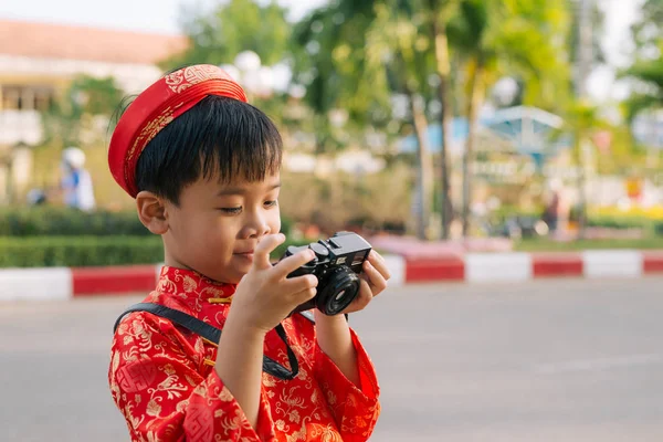 Child with digital compact camera outdoors. Cute little Vietnamese boy in ao dai dress smiling. Tet holiday