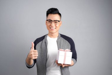 Bir hediye tutarak ve gri arka plan üzerinde izole başparmak vazgeçerek genç adam