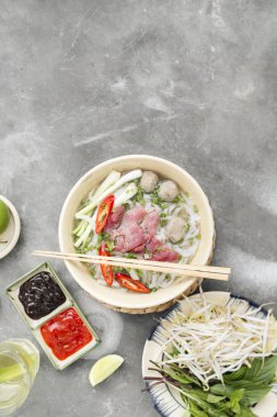 Geleneksel Vietnamca otlar, et, Pirinç Noodle Pho bo çorba suyu. Pho bo chopsticks, kase kaşık. Metin için yer. Üstten Görünüm. Ahşap masa arka plan Asya yemek Pho bo. Vietnamca çorbası