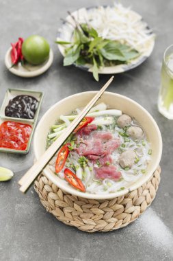 Geleneksel Vietnamca otlar, et, Pirinç Noodle Pho bo çorba suyu. Pho bo chopsticks, kase kaşık. Metin için yer. Üstten Görünüm. Ahşap masa arka plan Asya yemek Pho bo. Vietnamca çorbası