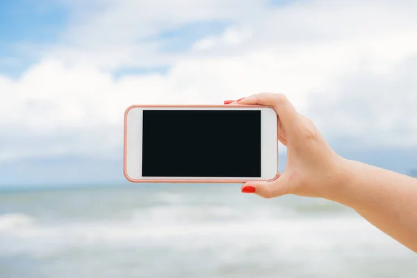 女性の手の背景に海とビーチで空白のスマート フォンに水平方向の画面の表示 ストック写真