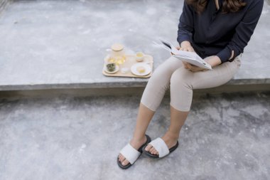 Genç ve güzel kız bir kitap okuma ve çay içme yaz Teras katta oturuyor