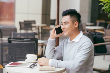 Bir kafede terasta açık havada oturma ve bir fincan - görüntü tutarak cep telefonunda konuşan adam