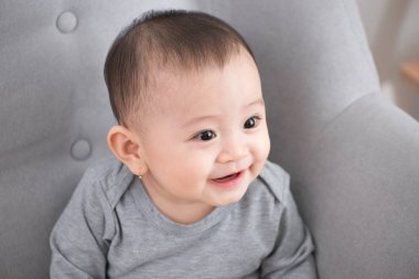 Portre portre sevimli gülüyor, kamera, doğal pencere ışık, yaşam tarzı uzak arıyor kanepede oturan siyah gözlü bebek kız gülümseyerek çok güzel