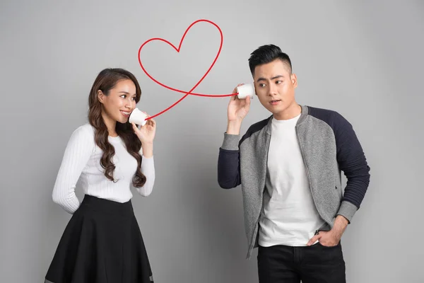 Joven asiático pareja con lata teléfono aislado en gris fondo — Foto de Stock