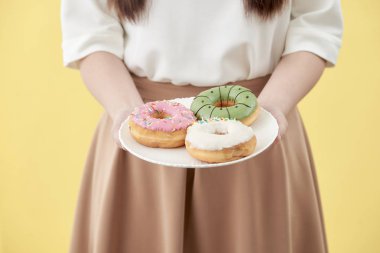 Asyalı kız göstermek ve plaka lezzetli lezzetli aromatik donuts tam izole gülümseme yüzüme holding.