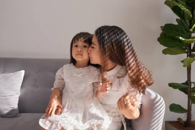 Tatlı küçük kız sarılma ve evde kanepede otururken yanak onu güzel genç anne öpüşme