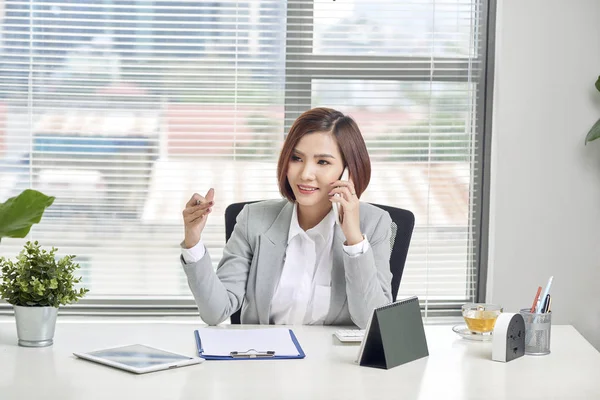 Cheerful Asian Female Talking Mobile Phone While Sitting Desk Laptop — Stock Photo, Image