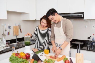 Mutlu genç çift öğle yemeği için sebze yemek hazırlarken kapalı modern mutfakta eğlenin