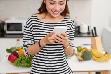pişirme sırasında akıllı telefon kullanan mutlu genç kadın