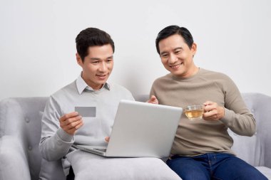 Bir kredi kartına parmak işaret ve oturma odasında kutluyor iken dizüstü bilgisayar tutan iki heyecanlı genç erkek portre