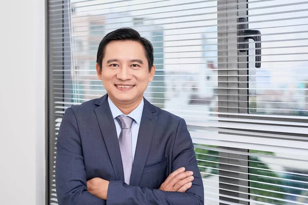 Single confident and handsome male businessman in blue suit and necktie with grin leaning on window outdoors