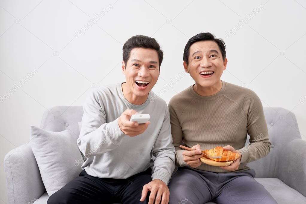 Men sitting on couch watching movie on television together at home.